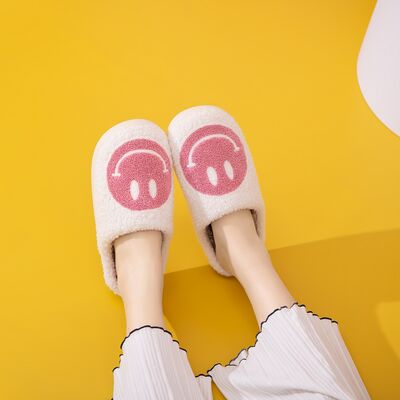 Pair of pink smiley face slippers with white faux fur, side view