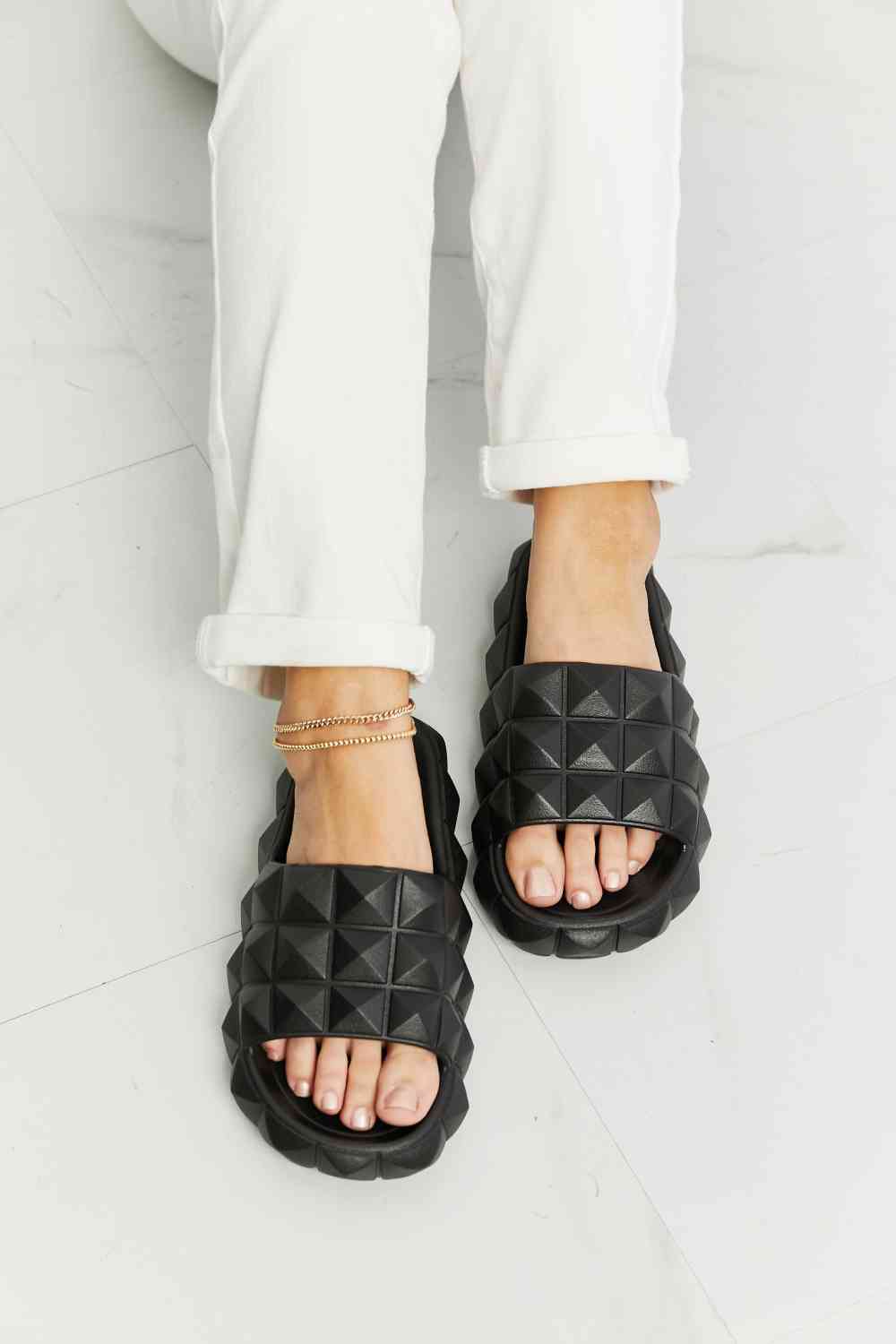 Black 3D stud slide sandals with platform sole, angled pair view